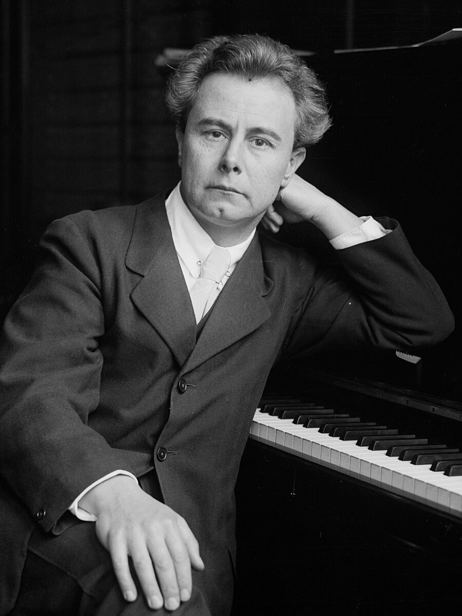 Man sitting leaning on piano in suit.
