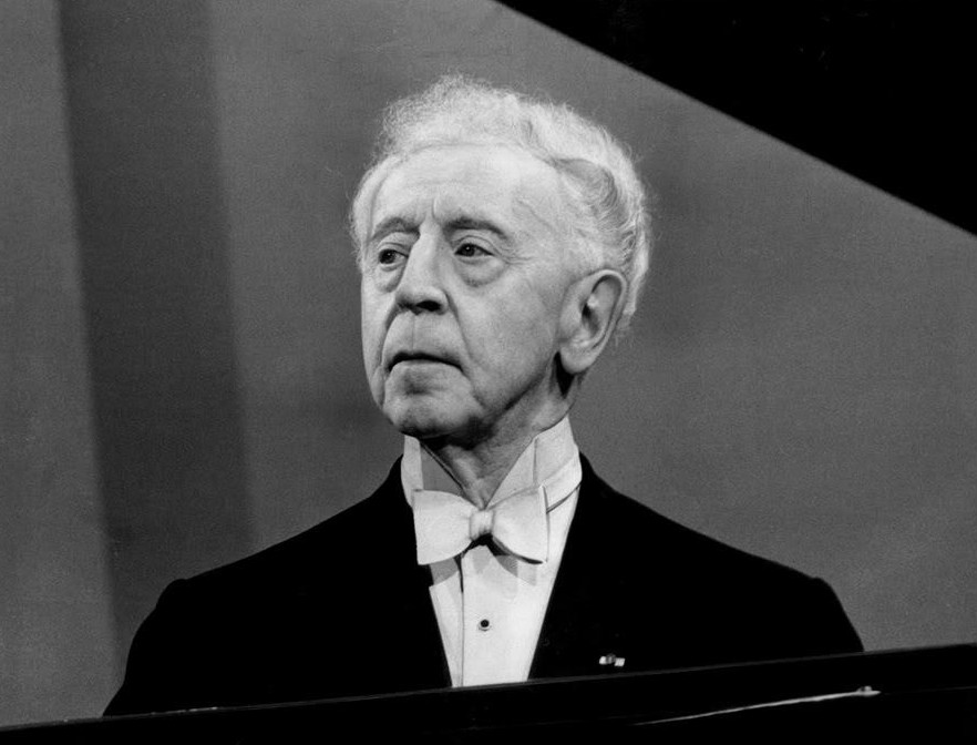 Older man with white bowtie looking above a piano.