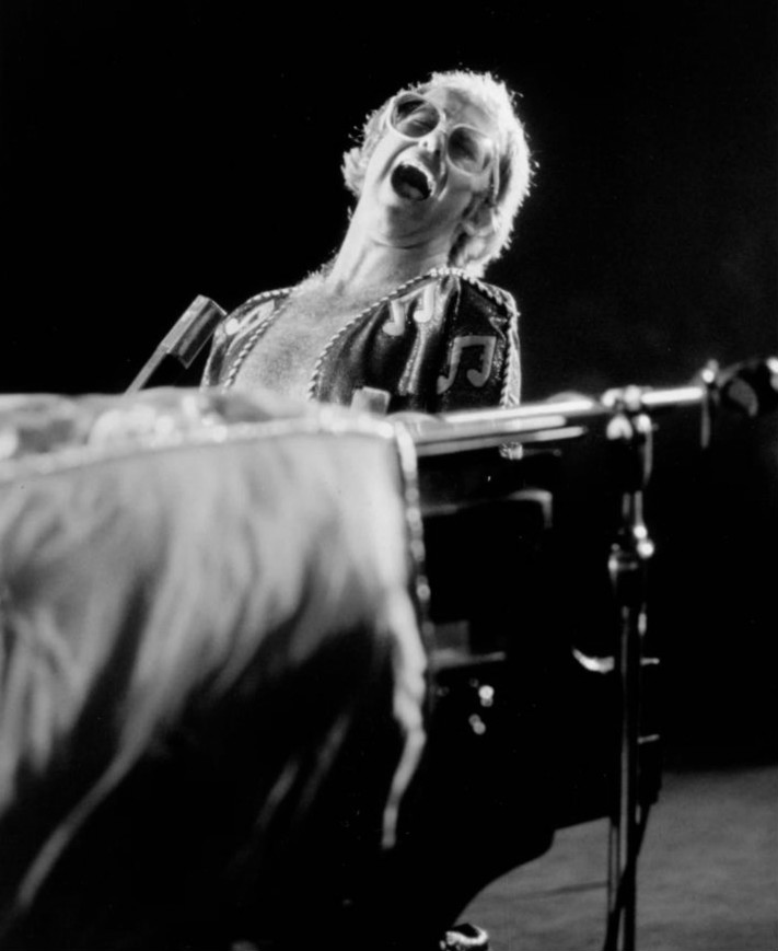 Elton John: Black and white photo of man in glasses singing passionately at the piano.