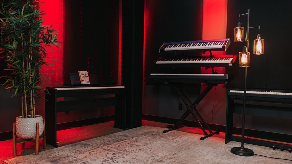 Red lighted studio with keyboards, lamp stand, and ficus plant.