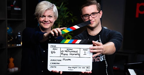 How good is Pianote? Personalized attention through weekly Q&A sessions. Lisa and Sam holding a clapper for a video they're filming.